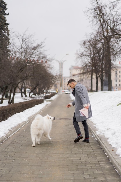 Boy friend with a bouquet of pink flowers hydrangea waiting for his girl friend and walking and playing with a dog. outdoors while snow is falling. Valetnine`s day concept, wedding proposal.
man goes