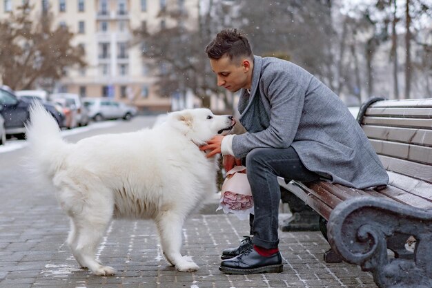 Boy friend with a bouquet of pink flowers hydrangea waiting for his girl friend and walking and playing with a dog. outdoors while snow is falling. Valetnine`s day concept, wedding proposal.
man goes