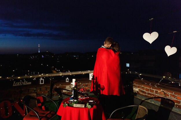 Boy and girl hug each other tender standing on the rooftop in the rays of evening lights 