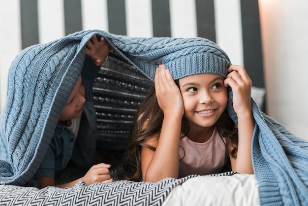 Free photo boy and girl lying under the woven blanket on bed