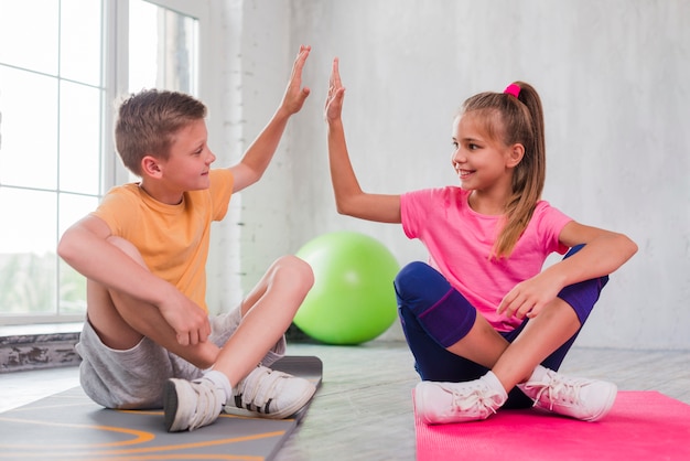 Boy and girl sitting on exercise mat giving high five