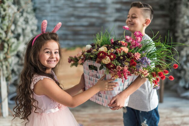バニーの耳の中の女の子に花を持つバッグを与える少年