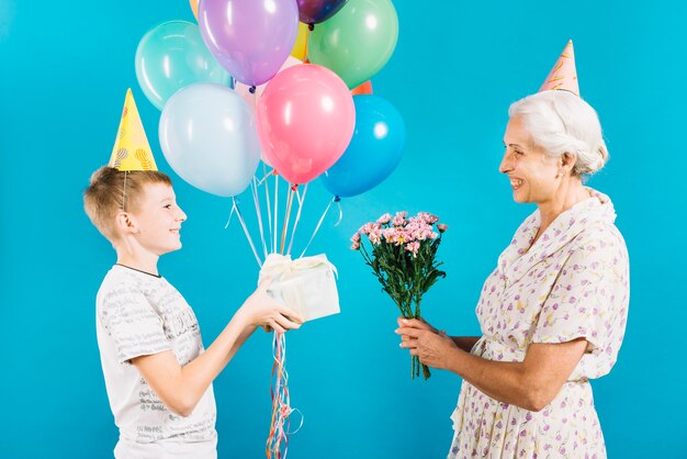 青い背景で幸せな祖母に誕生日の贈り物を与える少年