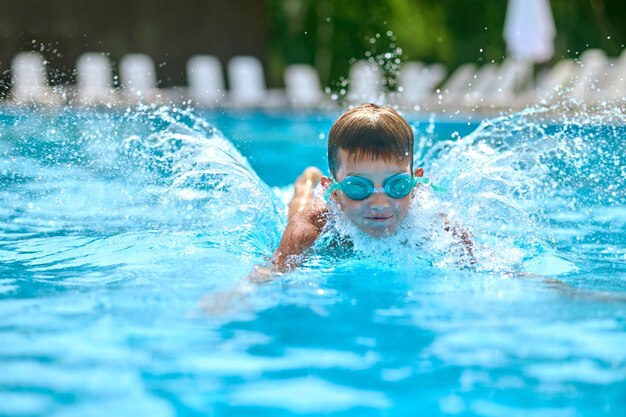 プールで水しぶきを上げて泳いでいるゴーグルの少年