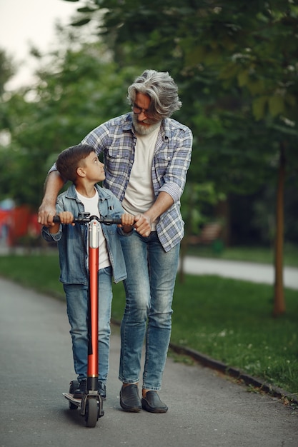 Boy and grandfather are walking in the park. Old man playing with grandson. Child with scooter.