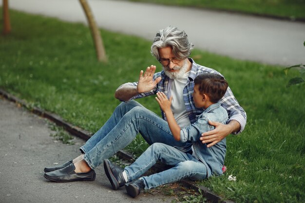 Boy and grandfather are walking in the park. Old man playing with grandson. Family sitting on a grass.