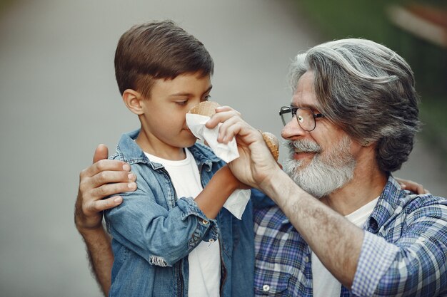 Boy and grandfather are walking in the park. Old man playing with grandson. Family with ice cream.