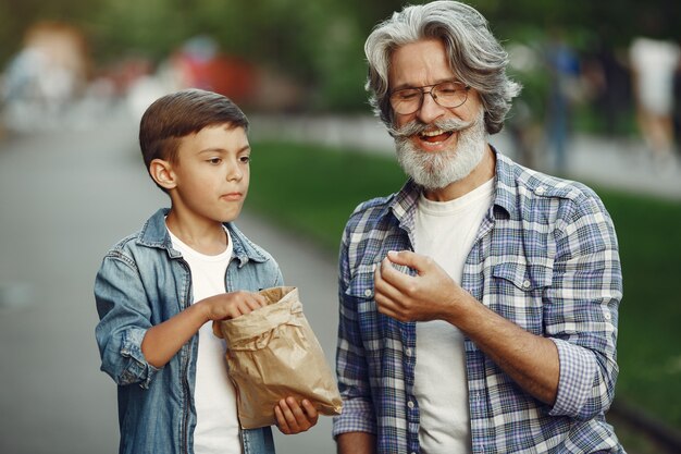 Boy and grandfather are walking in the park. Old man playing with grandson. People eat popcorn.