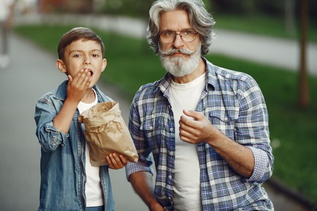 Boy and grandfather are walking in the park. Old man playing with grandson. People eat popcorn.