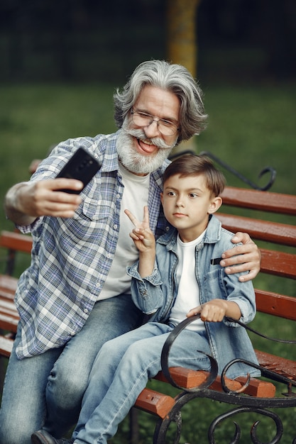 Ragazzo e nonno seduto su una panchina. famiglia nel parco. uomo anziano che gioca con il nipote. il nonno usa un telefono.