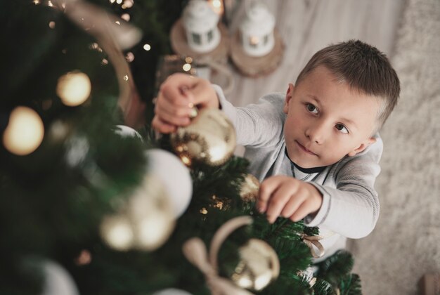 Мальчик вешает рождественские украшения на елку