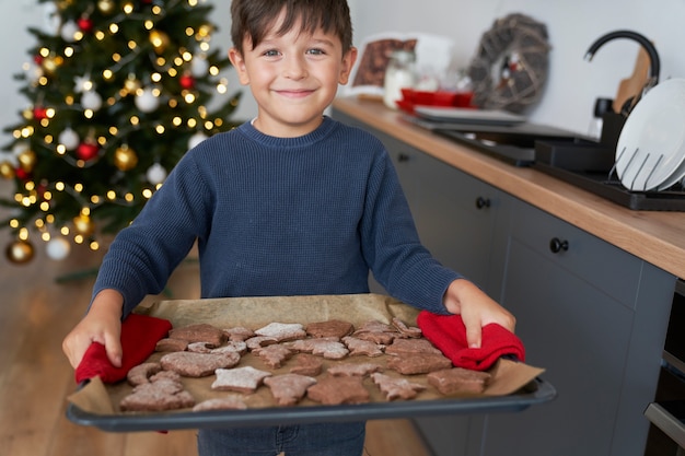 自家製ジンジャーブレッドクッキーがいっぱい入ったトレイを持っている少年