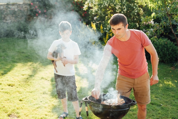 Boy holding dog standing near his father preparing food in park