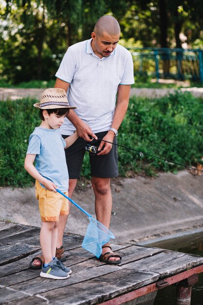 Boy holding fishing net standing with his father on pier