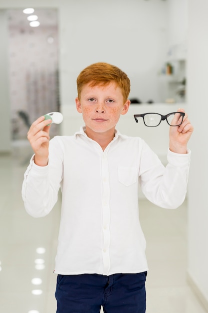 Boy holding plastic container of contact lenses and eyeglasses looking at camera