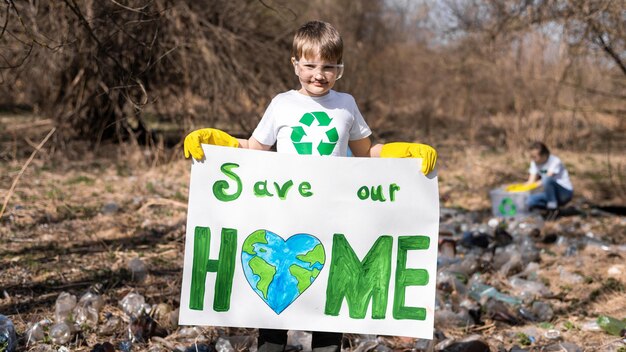 Мальчик держит плакат в защиту экологии на сборе пластикового мусора