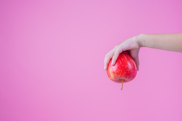Boy holds and eats red apples on a pink background.