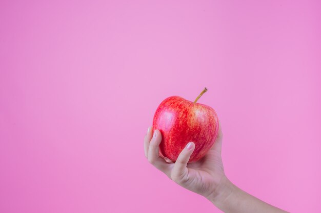 Boy holds and eats red apples on a pink background.