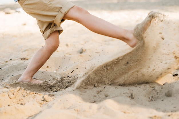 Мальчик пинает песок на пляже