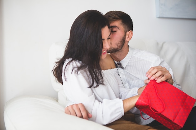 Boy kissing his girlfriend on the cheek while she opens a red bag