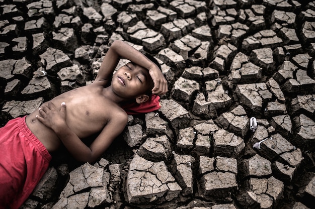 Free photo the boy lay flat, laying his hands on the belly and forehead on dry soil.