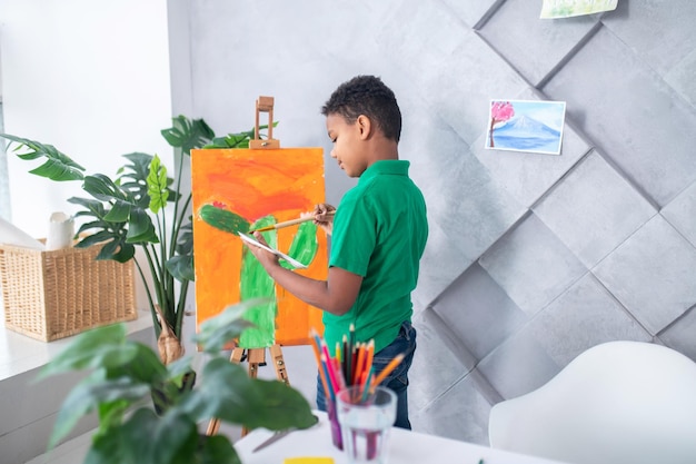 Boy looking at palette standing near easel