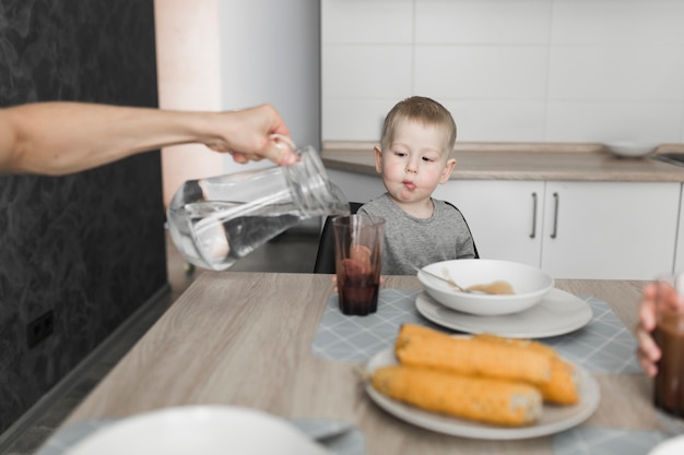 朝食でガラスに水を注ぐ人を見ている少年