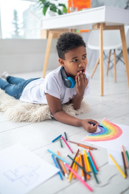 Boy lying on floor drawing yawning looking to side