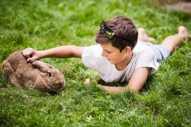 Boy lying on green grass loving his rabbit 