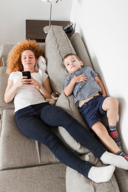スマートフォンを使って母親とソファーに横たわっている少年