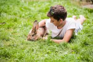 Free photo boy lying with his pet rabbit on green grass