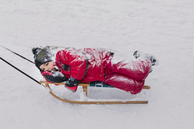 Ragazzo che si trova sulla slitta di legno sul paesaggio nevoso alla stagione invernale