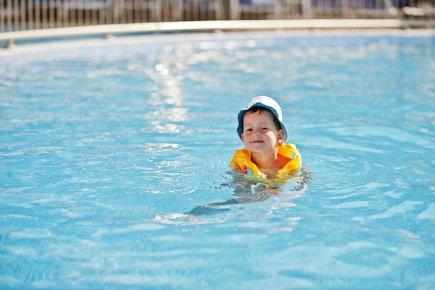 Мальчик в панаме и детский спасательный жилет купаются в бассейне