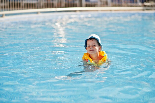Мальчик в панаме и детский спасательный жилет купаются в бассейне