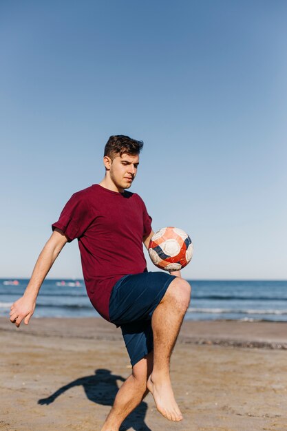 Мальчик играет в футбол на пляже