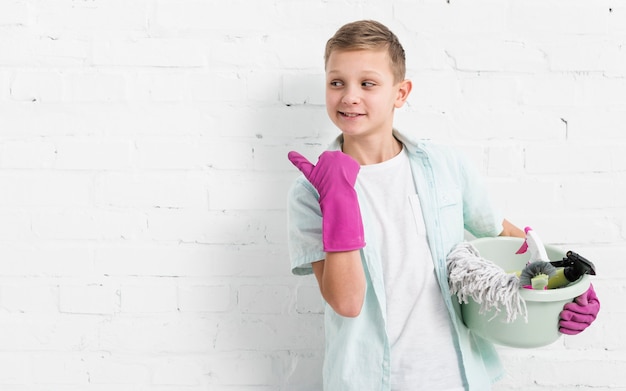 Free photo boy pointing while holding cleaning products with copy space