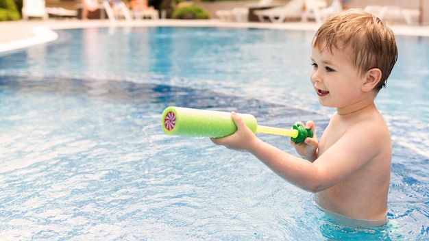 Foto gratuita ragazzo in piscina giocando con la pistola ad acqua