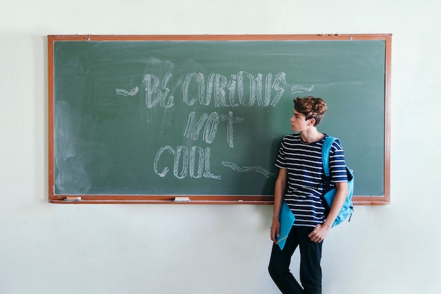 Free photo boy posing at the blackboard with backpack and folder