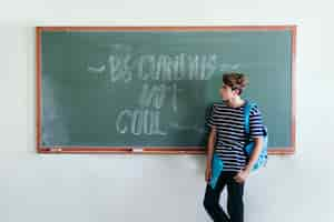 Free photo boy posing at the blackboard with backpack and folder