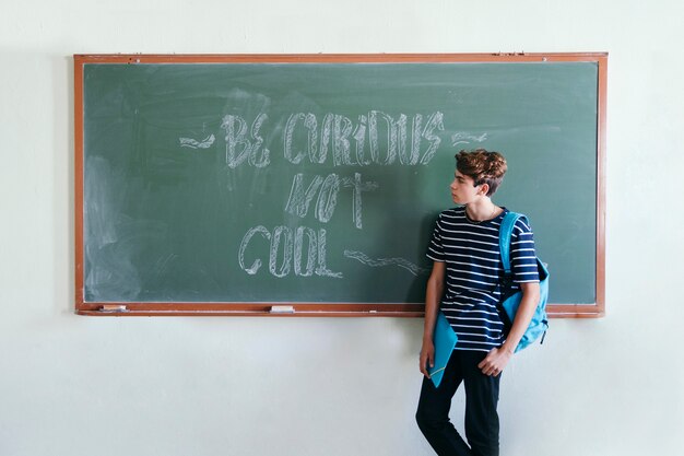 Boy posing at the blackboard with backpack and folder