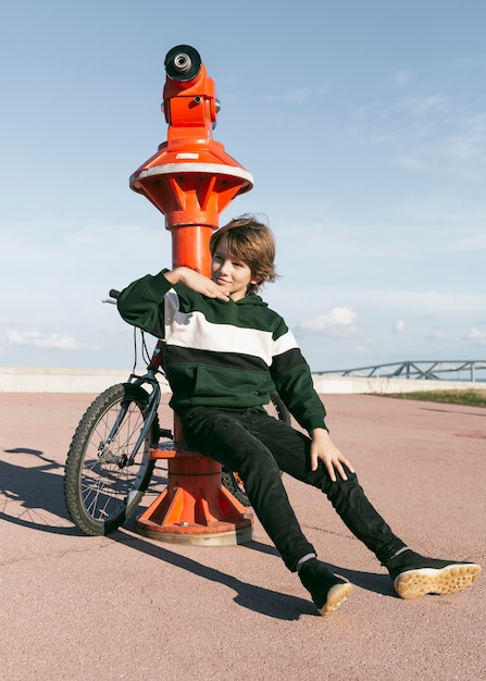 Boy posing next to telescope outdoors with his bike