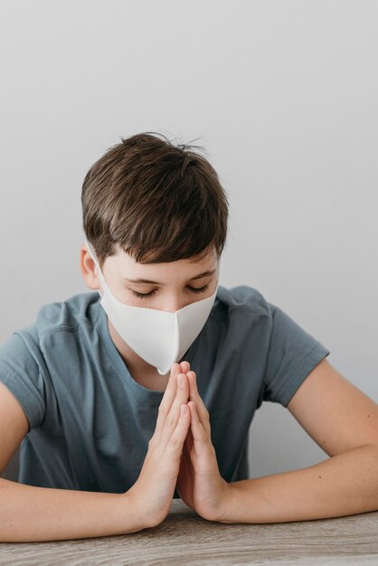 Foto gratuita ragazzo che prega mentre indossa una maschera medica al chiuso