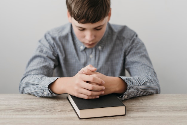 Бесплатное фото Мальчик молится, положив руки на библию