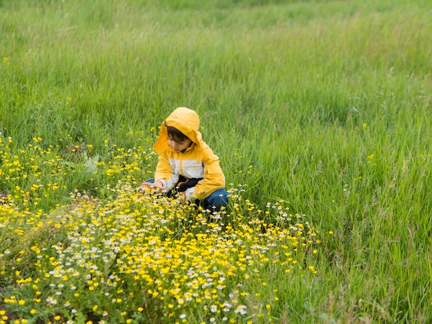 Free photo boy in raincoat picking flowers long shot