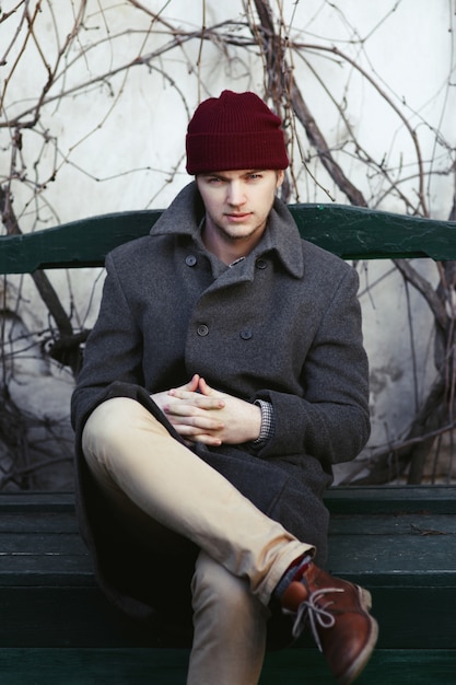 Foto gratuita il ragazzo in cappello rosso si siede sul banco verde