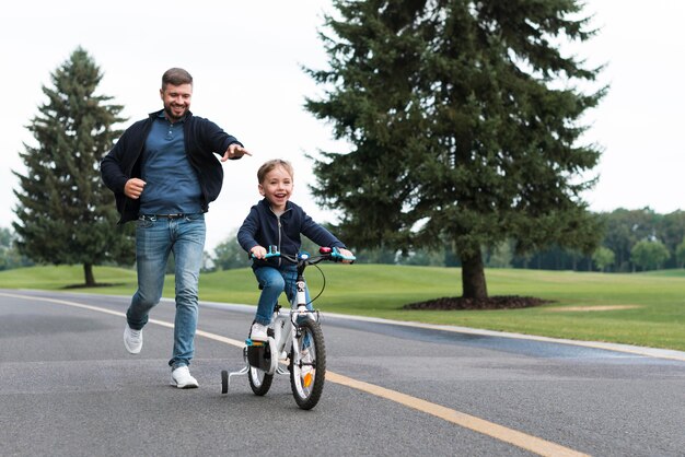 Мальчик катается на велосипеде в парке вместе со своим отцом