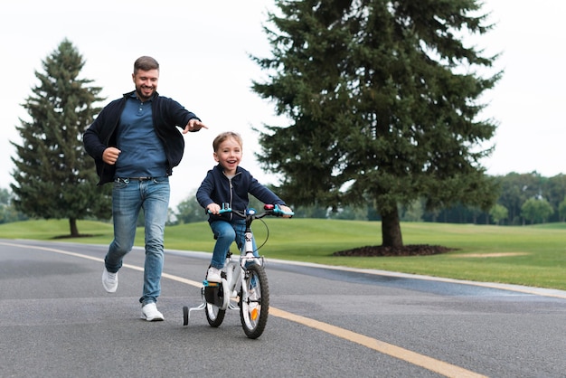Boy riding a bike in the park alongside his father