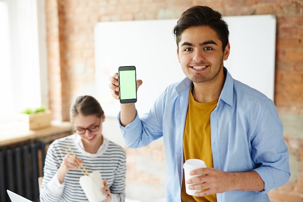 Boy showing a smartphone while holding a cup of coffee and girl eating with chopsticks