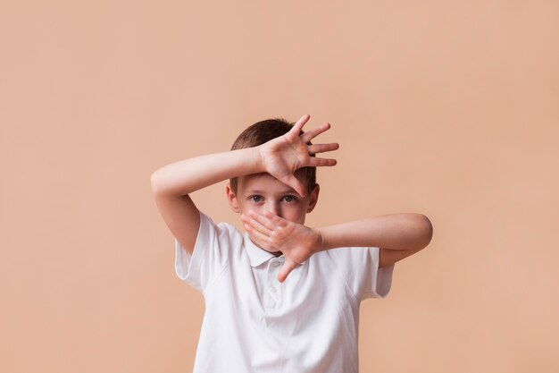 Мальчик показывает жест остановки, глядя на камеру на бежевом фоне