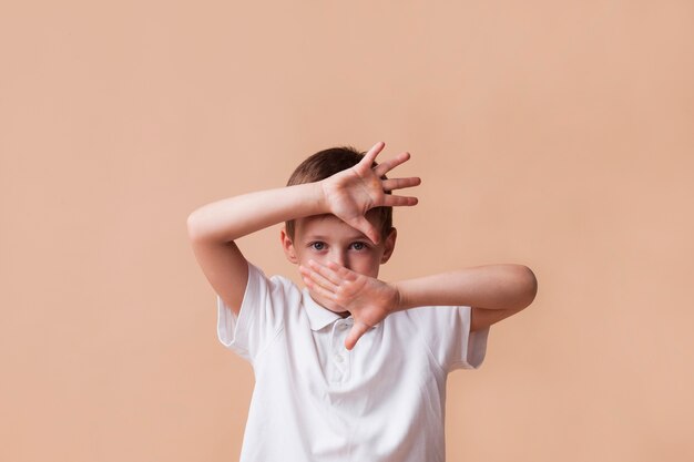 Boy showing stop gesture looking at camera on beige background